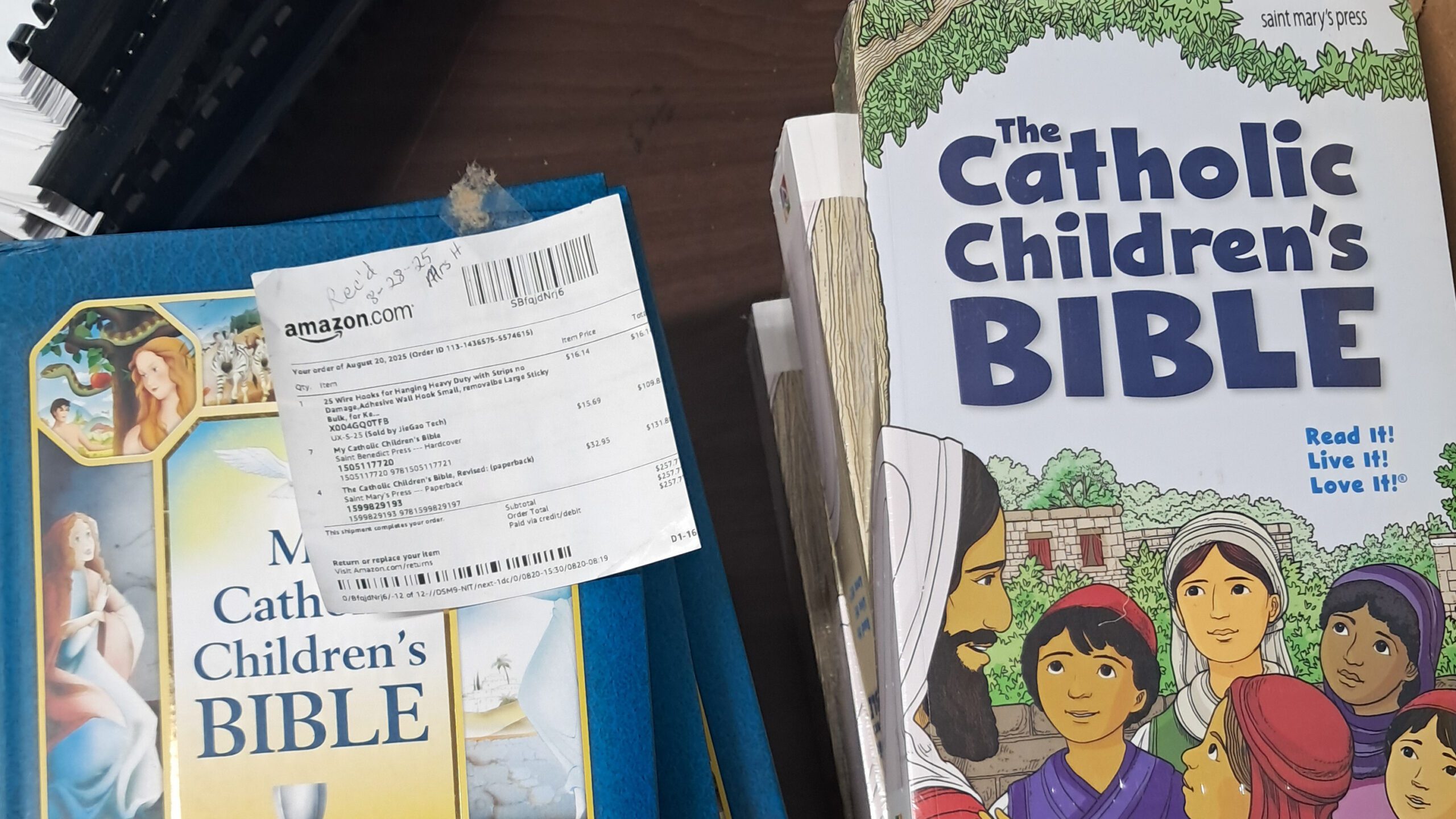 Catholic Children's Bible with a printed Amazon receipt on a blue folder on a desk.