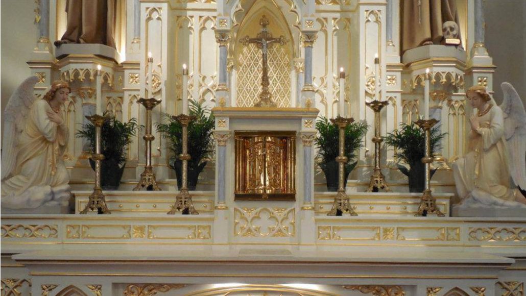 Ornate church altar with gold detailing, candles, and statues of angels on either side.