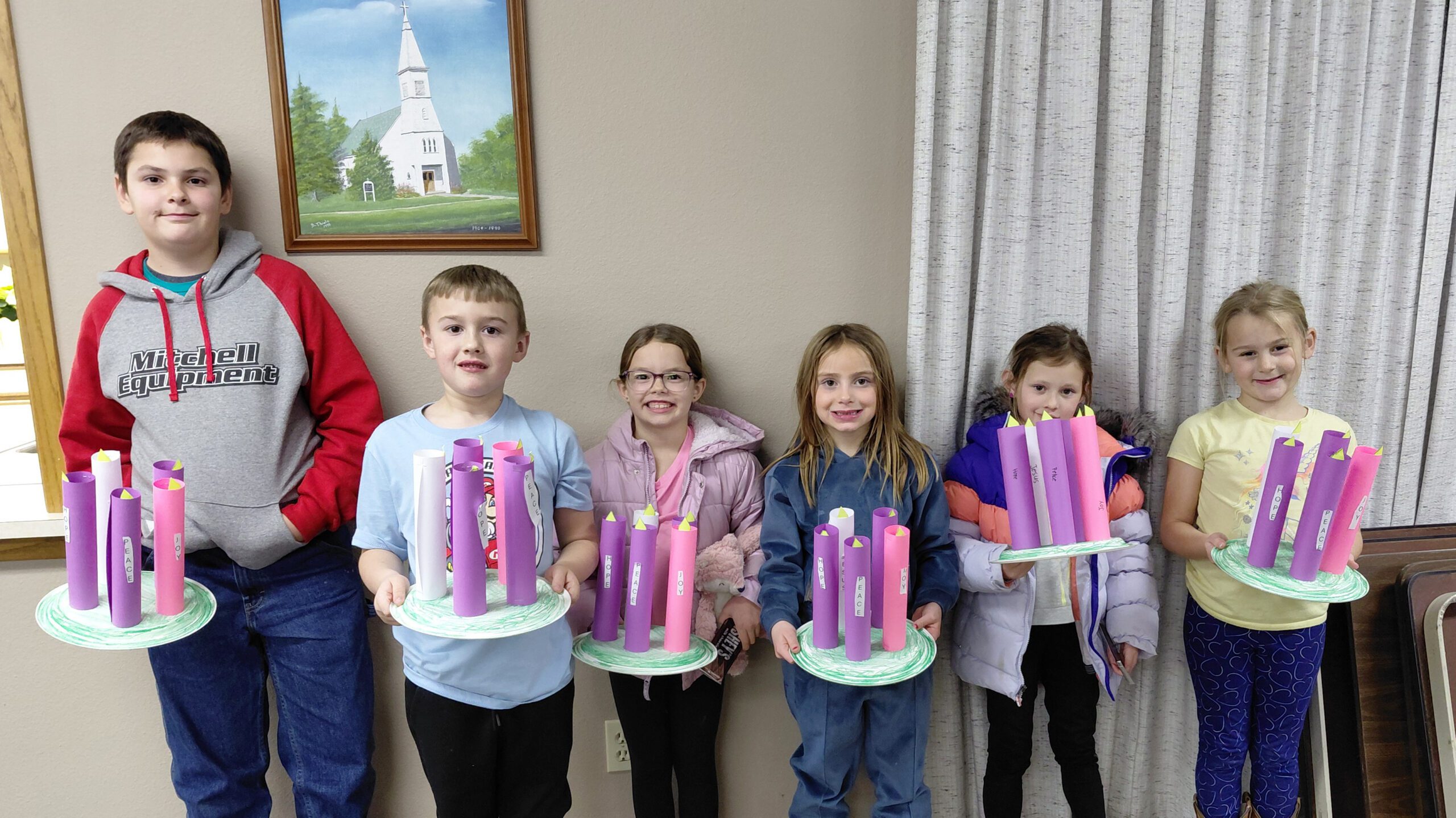 Six children stand indoors in a row, each holding a green plate with tall purple paper-tube crafts topped with yellow cones.